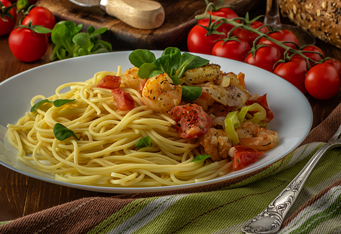 Spaghetti with shrimps, cherry tomatoes and spices on wooden background. Food background.